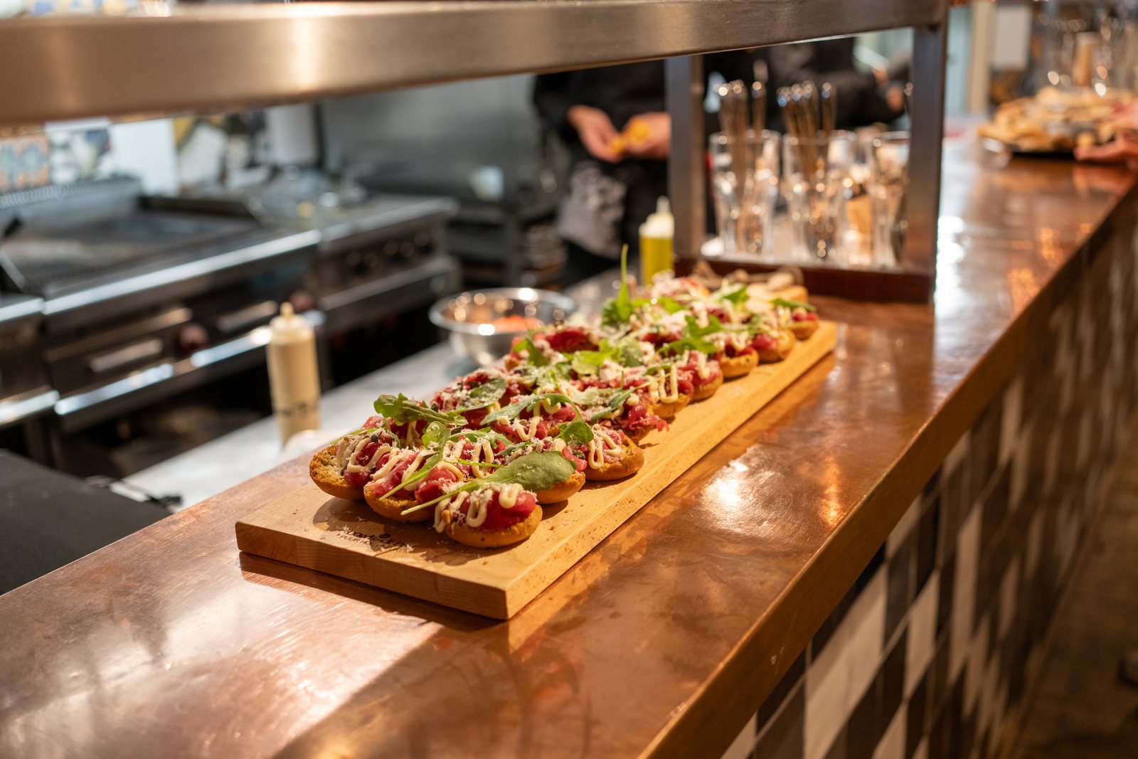 Doorgeefluik naar de keuken van DOKs Dining met hapjes op een plank op de koperen bar