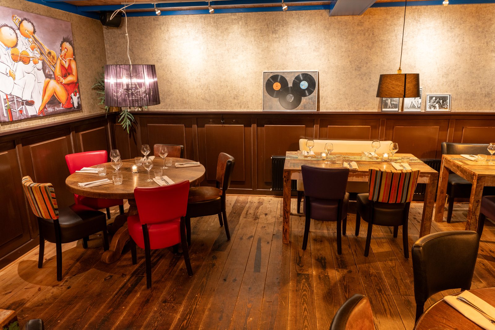 De Bijkeuken van DOKs Dining in Castricum met een ronde gedekte tafel, houten lambrisering en een schilderij van muzikanten