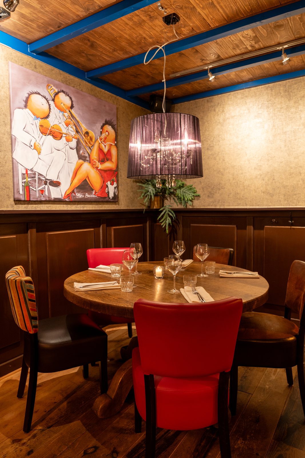 Ronde tafel met rode stoel in de Bijkeuken van DOKs Dining, onder het schilderij van muzikanten