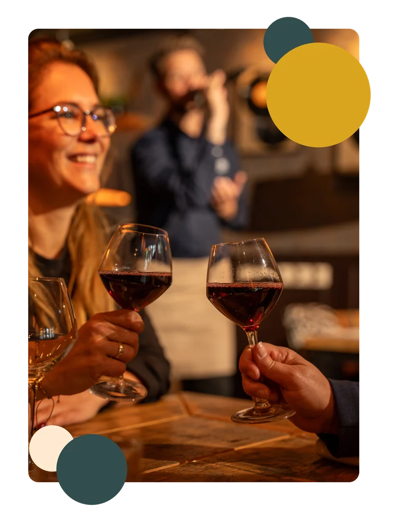 Twee gasten proosten met een glas rode wijn aan tafel bij DOKs Dining, op de achtergrond zingt de gastheer